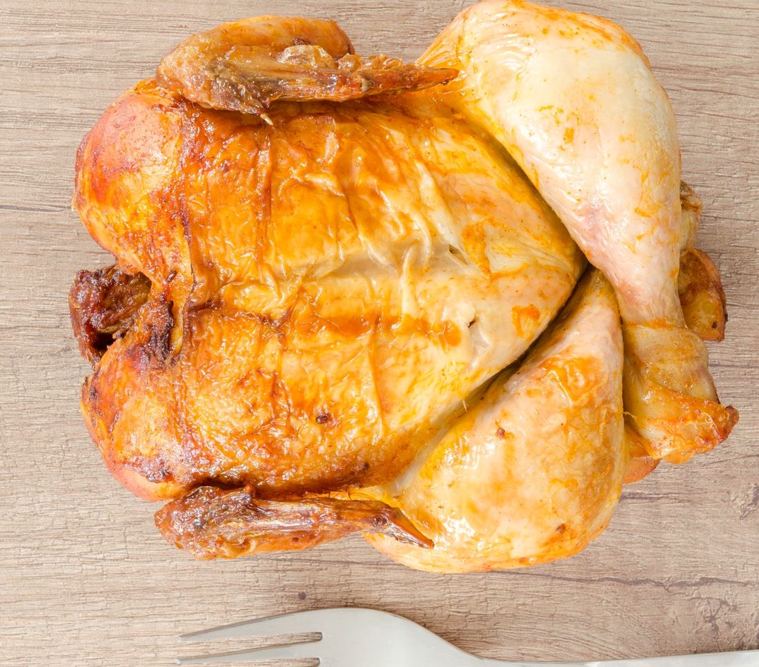 Frango inteiro assado, dourado, sobre mesa de madeira